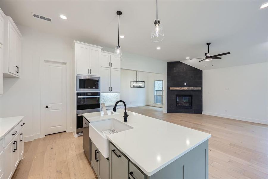 Kitchen featuring stainless steel appliances, a kitchen island with sink, light hardwood / wood-style flooring, white cabinets, and vaulted ceiling