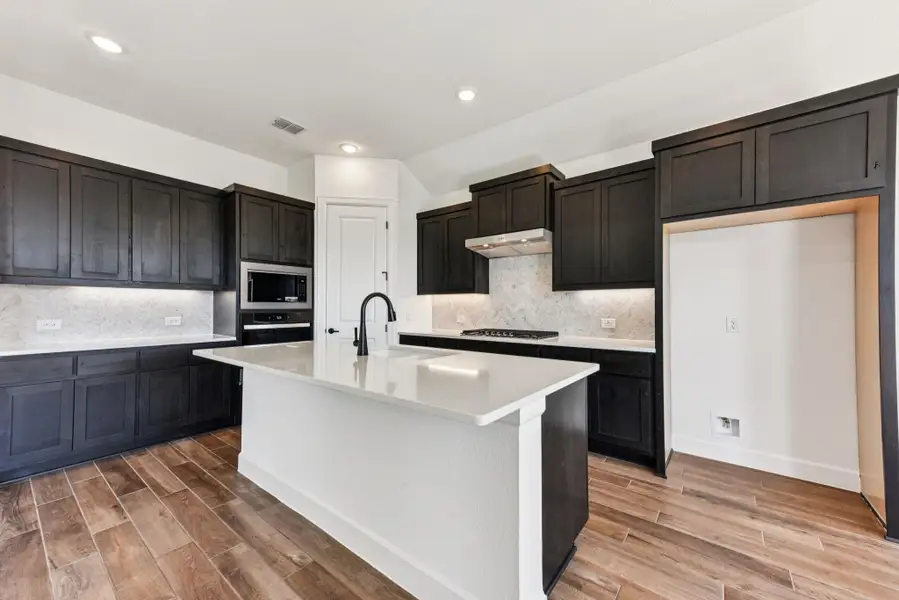 Kitchen with an island with sink, light wood finished floors, decorative backsplash, light stone countertops, and recessed lighting