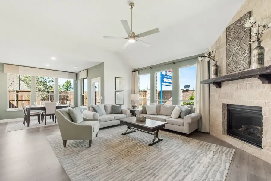 Open living room with vaulted ceiling, stone fireplace, ceiling fan, and dining area in background