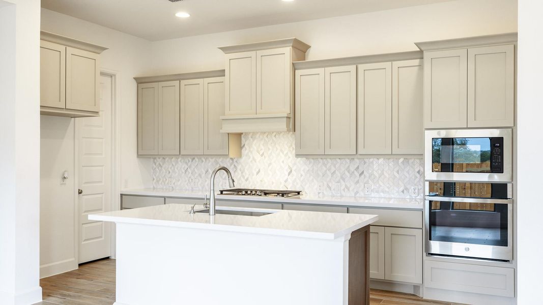 Kitchen with appliances with stainless steel finishes, decorative backsplash, light wood-style flooring, a kitchen island with sink, and light stone counters