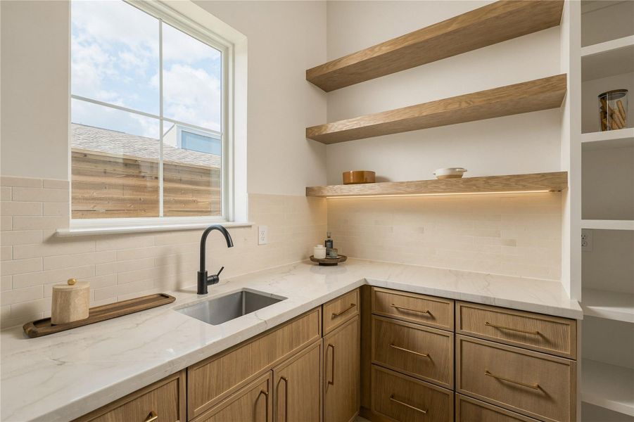 A discreet scullery-style pantry extends the kitchen’s functionality with generous prep space, additional cabinetry, open white oak shelving, and its own sink—keeping the main kitchen ready for entertaining.