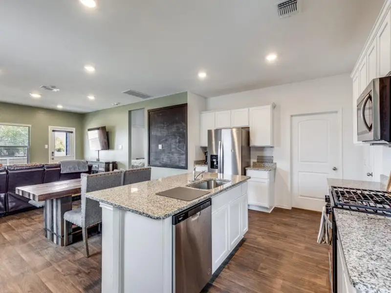 Kitchen with stainless steel appliances, white cabinetry, light stone countertops, recessed lighting, and open floor plan