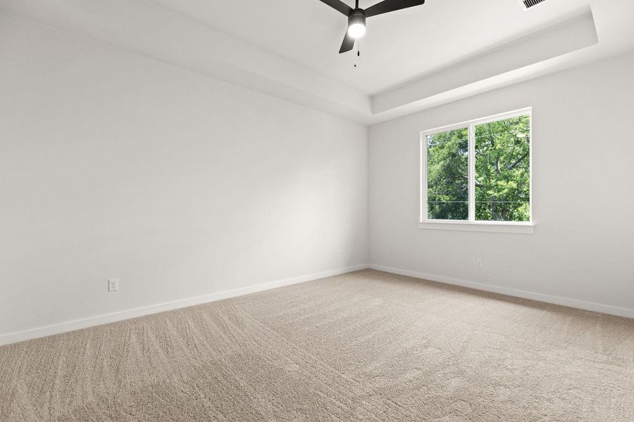 A spacious, naturally illuminated room boasts plush carpeting and a modern ceiling fan.