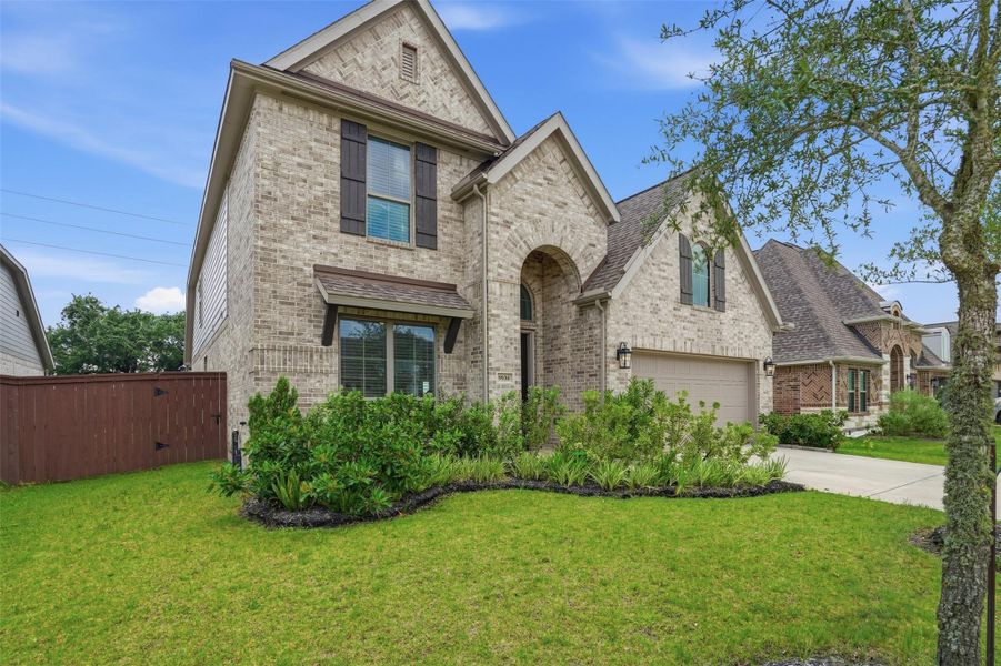 This is a two-story brick home with a gabled roof and attached two-car garage. It features a well-maintained lawn, landscaped garden beds, and a wooden privacy fence. The large windows and arched entryway enhance its curb appeal. This is a two-story brick home with a gabled roof and attached two-car garage. It features a well-maintained lawn, landscaped garden beds, and a wooden privacy fence. The large windows and arched entryway enhance its curb appeal.