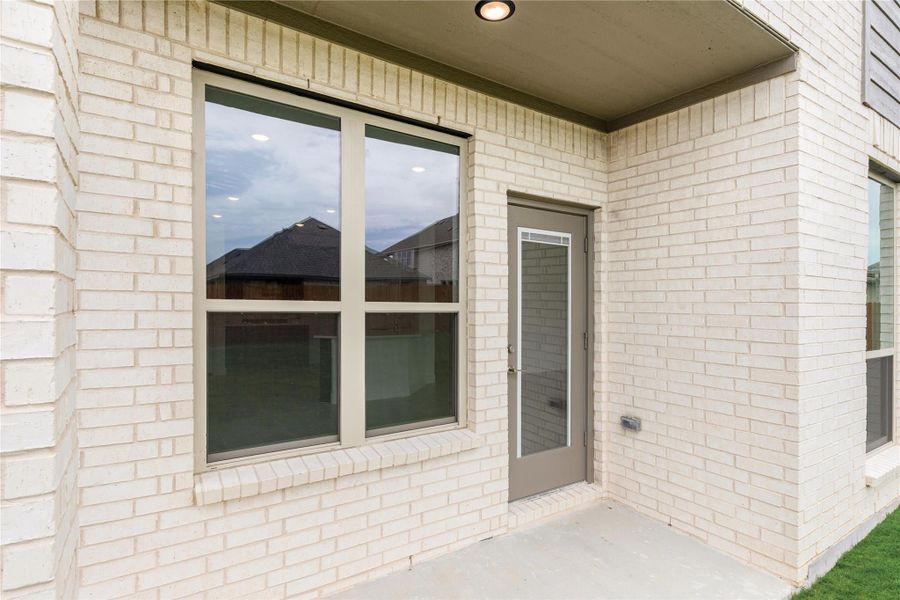 Covered patio entry with gray door and large windows on a cream brick home exterior. Covered patio entry with gray door and large windows on a cream brick home exterior.
