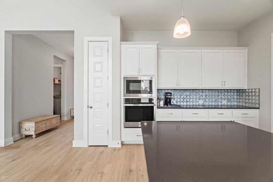Kitchen featuring white cabinetry, stainless steel oven, light wood-style flooring, tasteful backsplash, and built in microwave Kitchen featuring white cabinetry, stainless steel oven, light wood-style flooring, tasteful backsplash, and built in microwave
