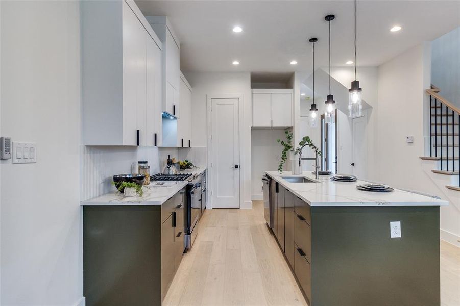 Kitchen featuring white cabinetry, gas range oven, sink, and a center island with sink