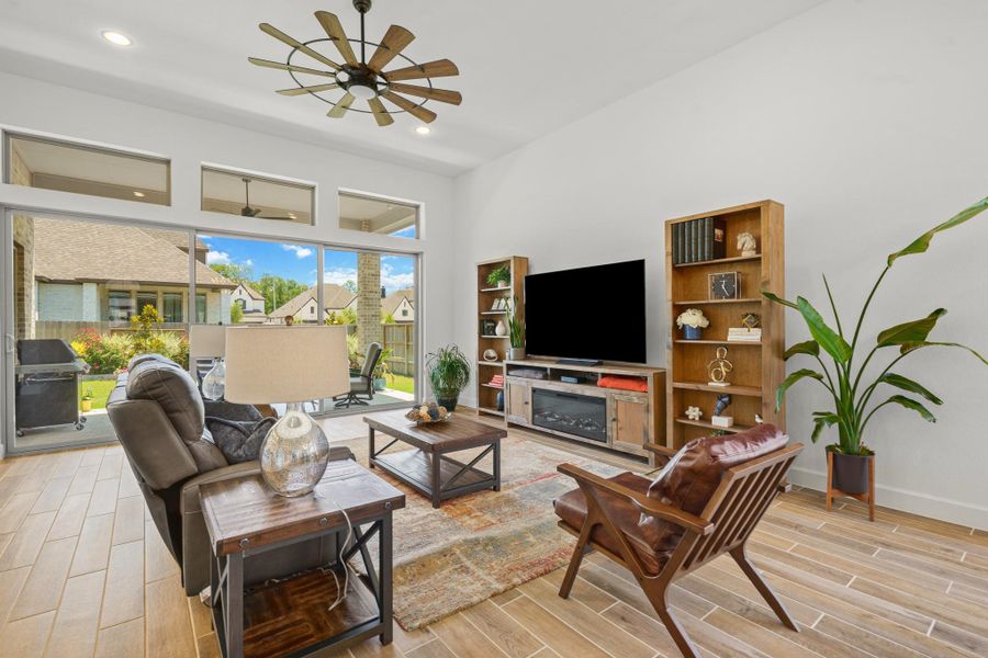 This bright, modern living room features large windows with a view of the beautifully landscaped backyard, wood-look tile flooring.