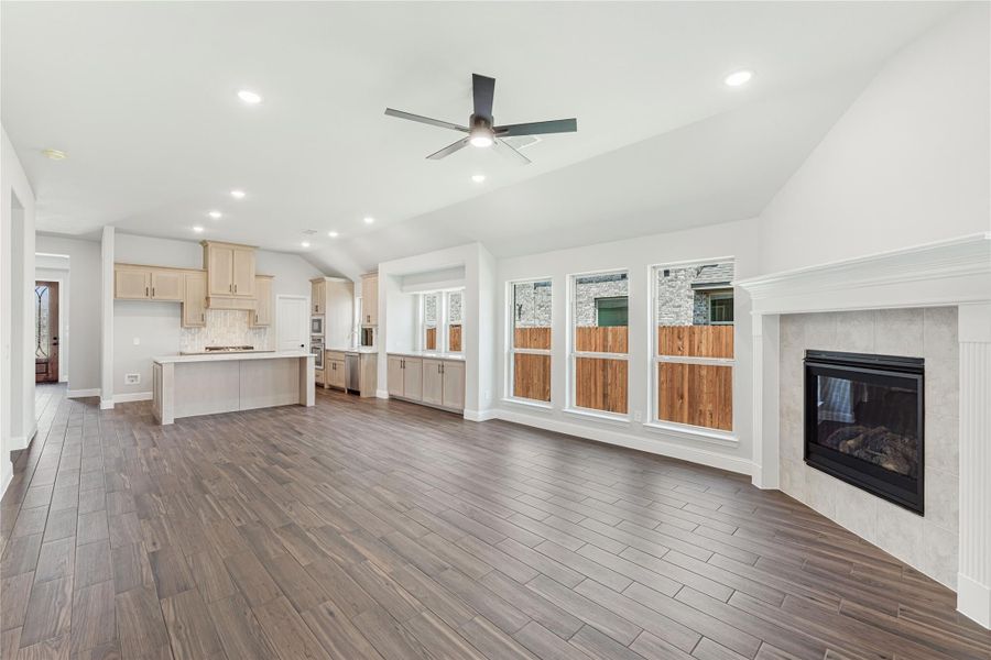 Open living area with tile fireplace, wood-look floors, and open kitchen with light cabinets and island Open living area with tile fireplace, wood-look floors, and open kitchen with light cabinets and island
