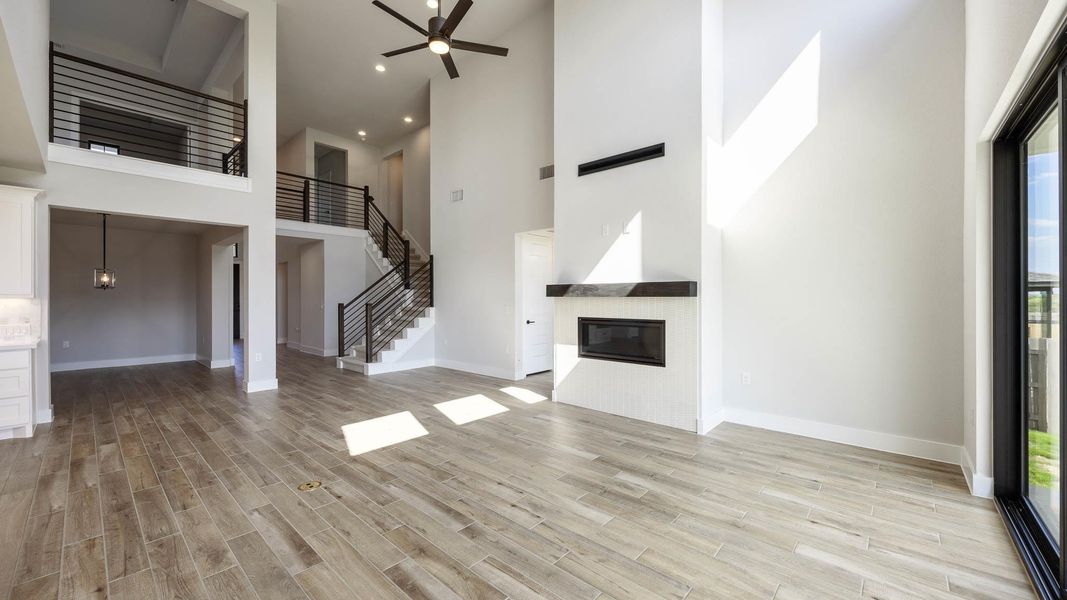 Unfurnished living room featuring a towering ceiling, a glass covered fireplace, ceiling fan, light wood finished floors, and recessed lighting