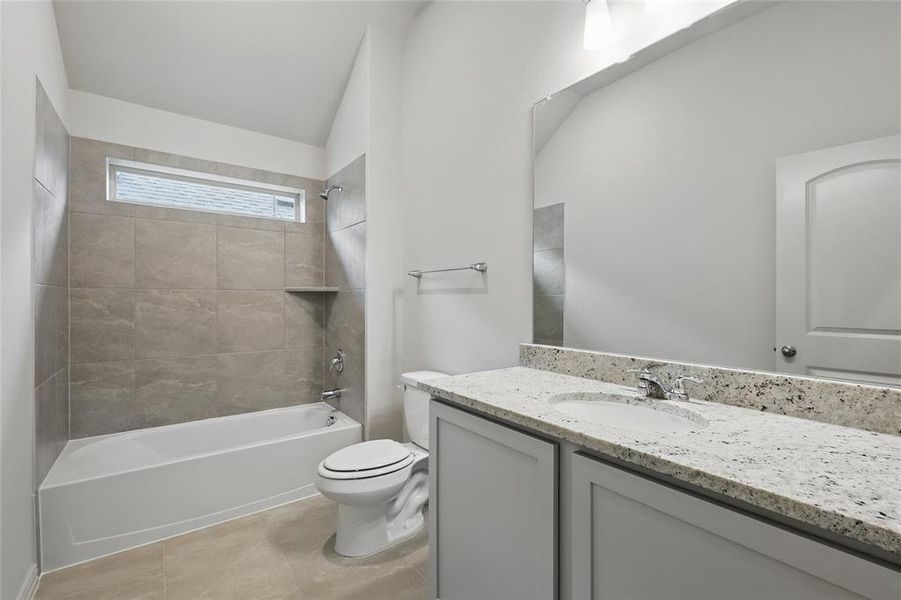 Bathroom featuring vanity, shower / bathtub combination, light tile patterned floors, and vaulted ceiling