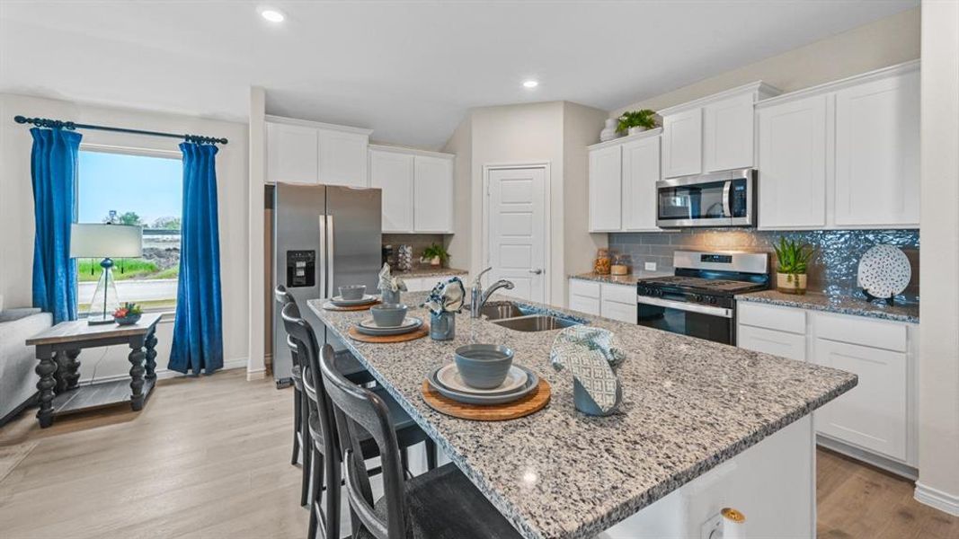 Kitchen with a breakfast bar, stainless steel appliances, white cabinets, light wood-style floors, and light stone counters Kitchen with a breakfast bar, stainless steel appliances, white cabinets, light wood-style floors, and light stone counters