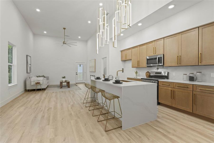 Kitchen featuring stainless steel appliances, a towering ceiling, plenty of natural light, a kitchen bar, and recessed lighting Kitchen featuring stainless steel appliances, a towering ceiling, plenty of natural light, a kitchen bar, and recessed lighting