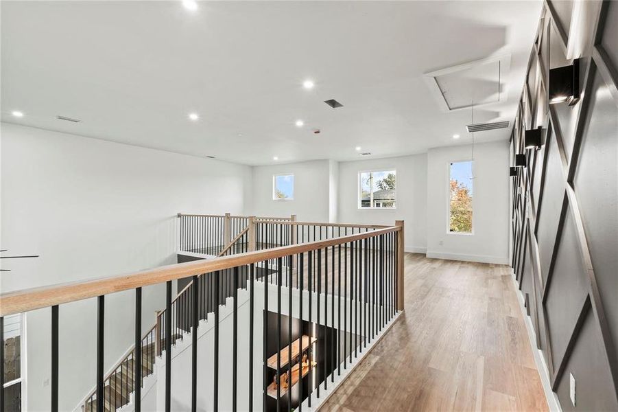 Open-concept upper level featuring wood-finish flooring, recessed lighting, a modern accent wall with sconce lighting, and a staircase with wood handrails and black metal balusters