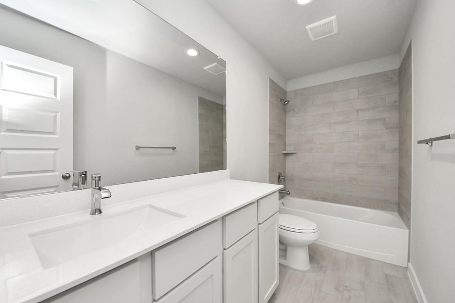Secondary bath features tile flooring, bath/shower combo with tile surround, light stained wood cabinets, beautiful light countertop. Sample photo of completed home with similar floor plan. Actual colors and selections may vary.