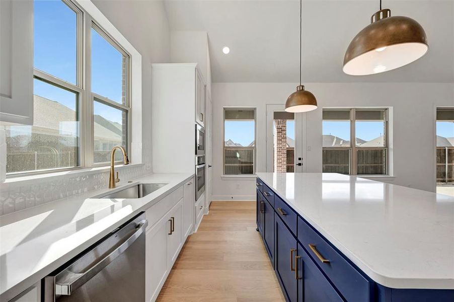 Kitchen featuring two tone cabinetry, stainless steel appliances, pendant lighting, light stone countertops, and light wood-style flooring Kitchen featuring two tone cabinetry, stainless steel appliances, pendant lighting, light stone countertops, and light wood-style flooring