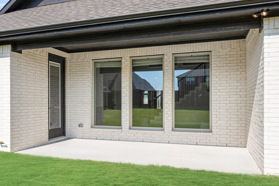 Covered back patio with concrete slab, white brick exterior, large windows, and back door entry Covered back patio with concrete slab, white brick exterior, large windows, and back door entry