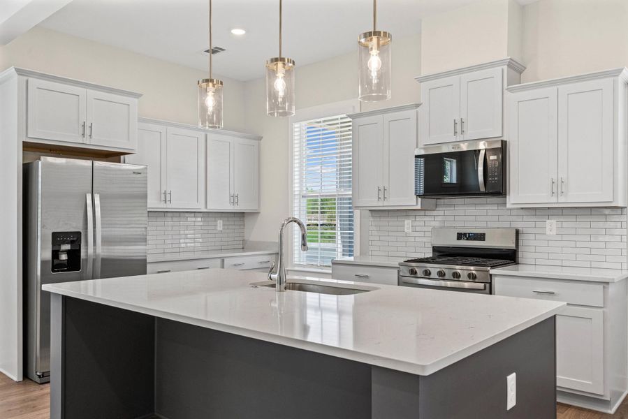 Kitchen featuring stainless steel appliances, an island with sink, two tone color scheme, light wood finished floors, and hanging light fixtures Kitchen featuring stainless steel appliances, an island with sink, two tone color scheme, light wood finished floors, and hanging light fixtures