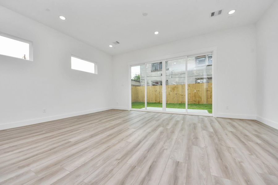This bright, spacious room features light wood flooring and large sliding glass doors that open to a fenced backyard, offering ample natural light and a seamless indoor-outdoor flow.