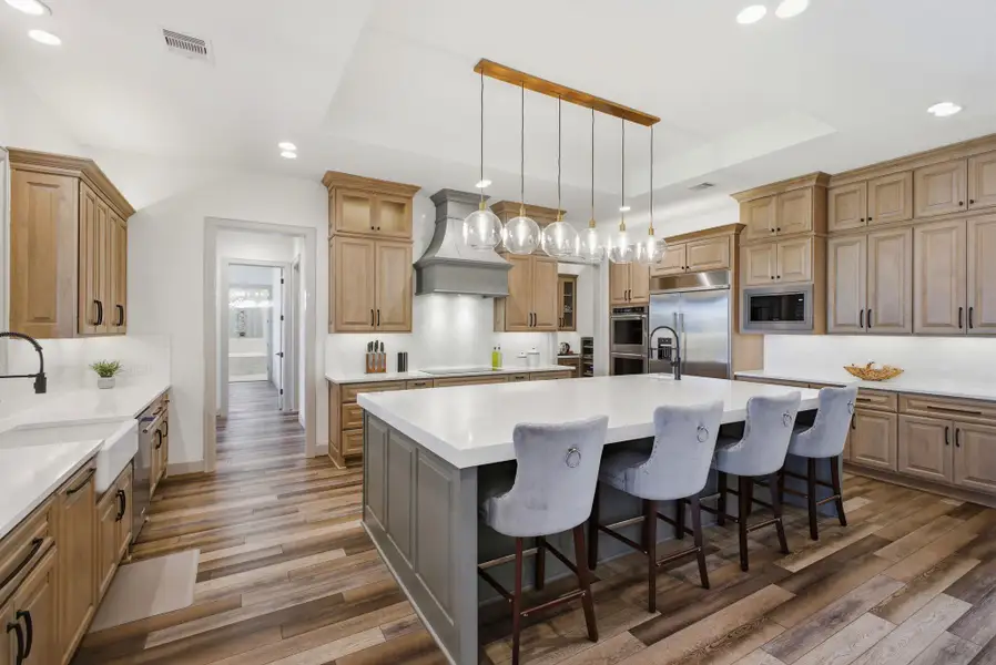 The kitchen features extensive cabinetry, a large central island with seating, white countertops, and stainless steel appliances