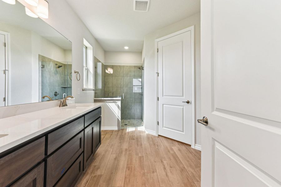Full bath featuring a shower stall, double vanity, and light wood-type flooring