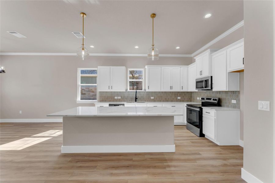 Kitchen with decorative light fixtures, white cabinets, stainless steel appliances, light wood-type flooring, and a center island