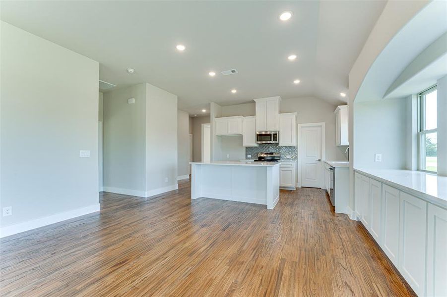 Kitchen featuring decorative backsplash, stainless steel appliances, light hardwood / wood-style flooring, white cabinetry, and lofted ceiling