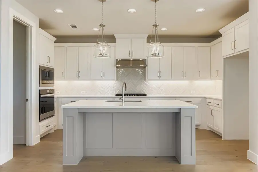 Kitchen featuring backsplash, pendant lighting, stainless steel appliances, a center island with sink, and white cabinets