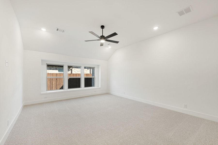 Empty bedroom with vaulted ceiling, ceiling fan, carpet flooring, and a triple window