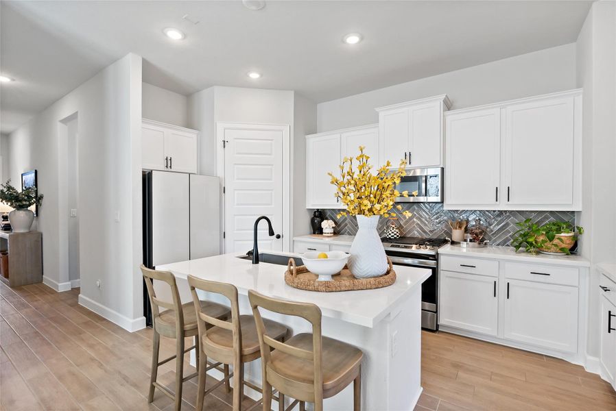 Kitchen with a breakfast bar area, a center island with sink, backsplash, white cabinets, and stainless steel appliances and walk in pantry