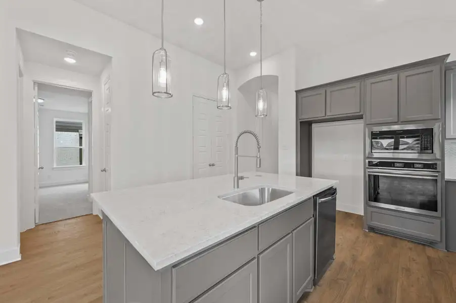 Kitchen with light stone countertops, gray cabinetry, a sink, stainless steel appliances, and dark wood-style floors