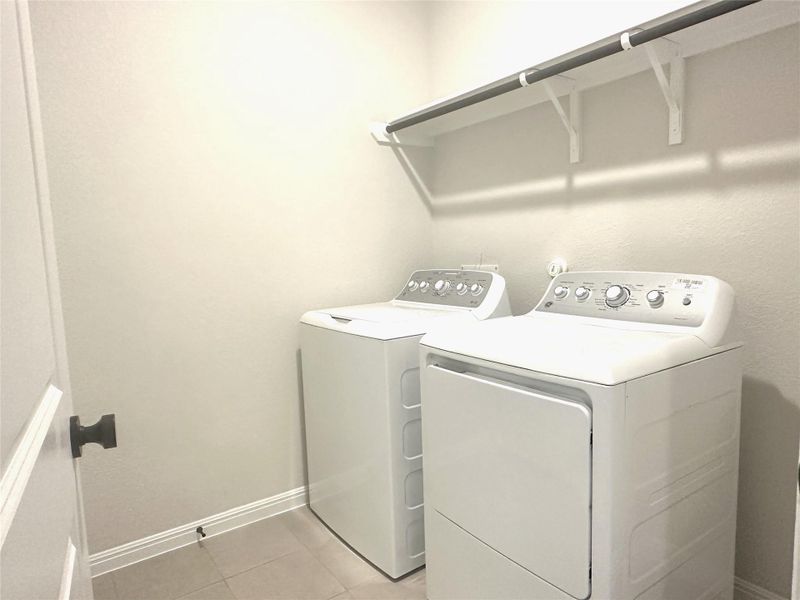 Washroom featuring washing machine and clothes dryer, light tile floors, and baseboards