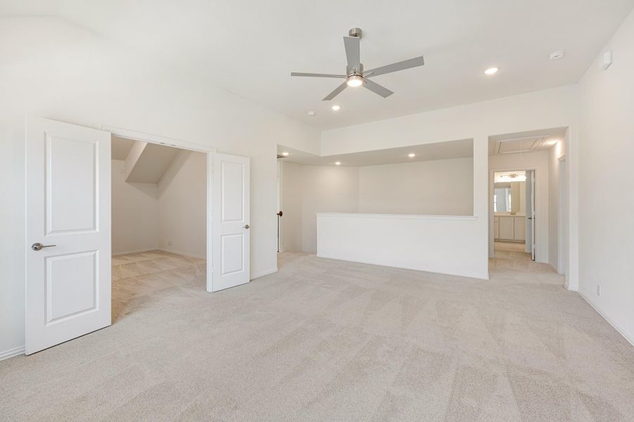 Spacious bedroom with ceiling fan, carpet flooring, walk-in closet, and ensuite bathroom doorway Spacious bedroom with ceiling fan, carpet flooring, walk-in closet, and ensuite bathroom doorway