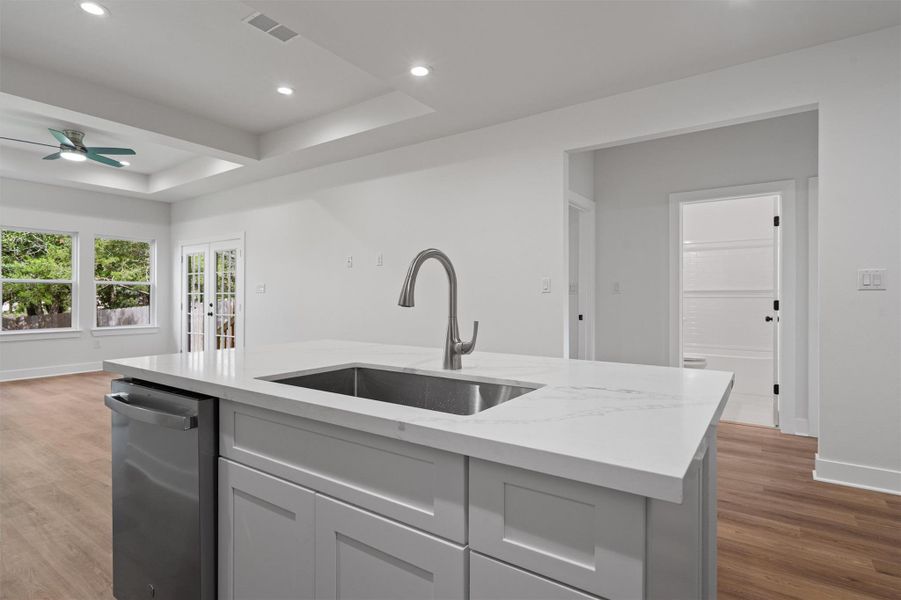 Kitchen island with a stainless steel sink, gooseneck faucet, and light-toned solid surface countertop