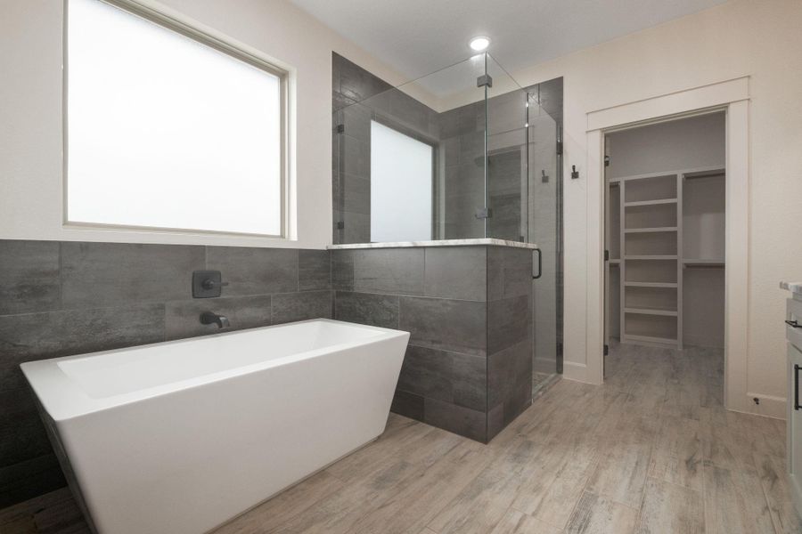 Bathroom with a soaking tub, a walk in closet, a stall shower, vanity, and light wood finished floors