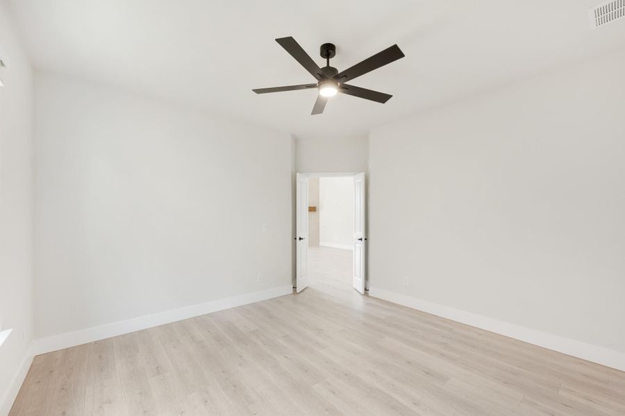 Empty bedroom with light wood floors, white walls, and a dark ceiling fan with light fixture