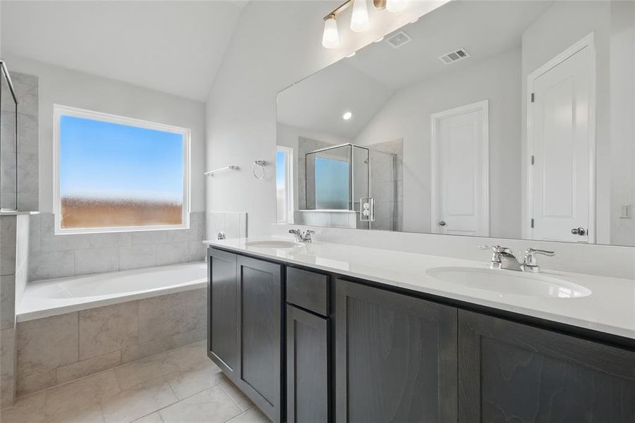 Bathroom featuring a stall shower, a garden tub, double vanity, lofted ceiling, and tile patterned floors Bathroom featuring a stall shower, a garden tub, double vanity, lofted ceiling, and tile patterned floors