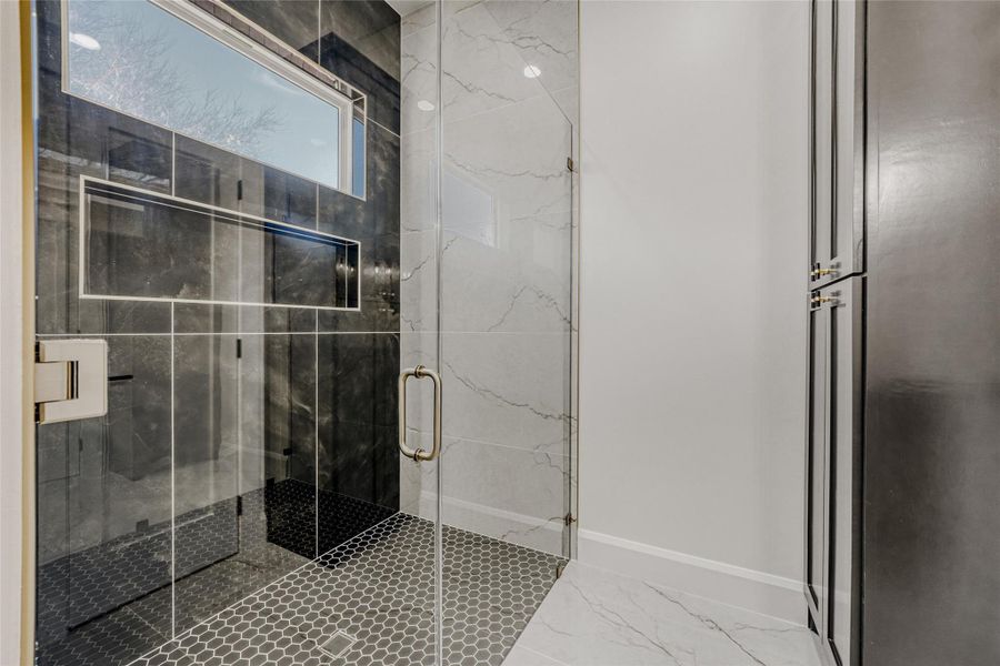 Enjoy a deluxe walk-in shower surrounded in beautiful tile with a clerestory window for natural light, plus adjacent linen built-ins.