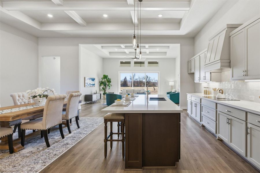 Kitchen featuring coffered ceiling, two tone color scheme, pendant lighting, a breakfast bar area, and a kitchen island with sink