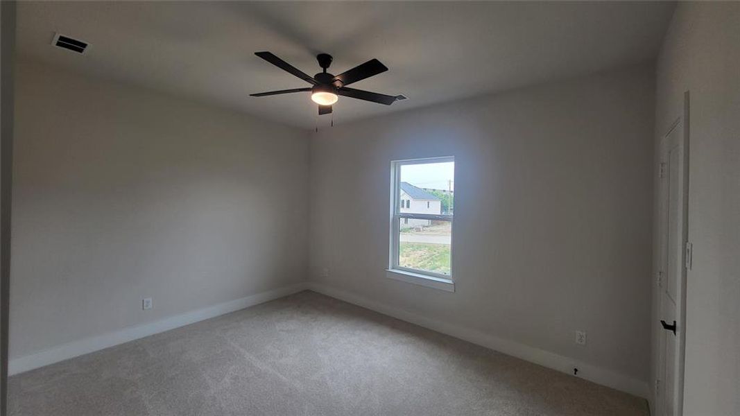 Carpeted spare room featuring baseboards, a ceiling fan, and visible vents