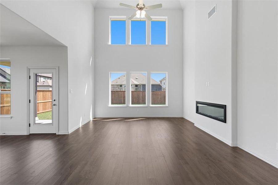 Unfurnished living room featuring a glass covered fireplace, a high ceiling, dark wood finished floors, and a ceiling fan Unfurnished living room featuring a glass covered fireplace, a high ceiling, dark wood finished floors, and a ceiling fan