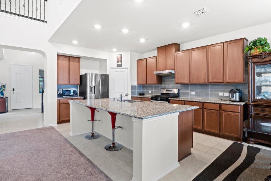 Expansive kitchen featuring a large island with a stone-finish countertop, rich wood cabinetry, stainless steel appliances, and tile flooring