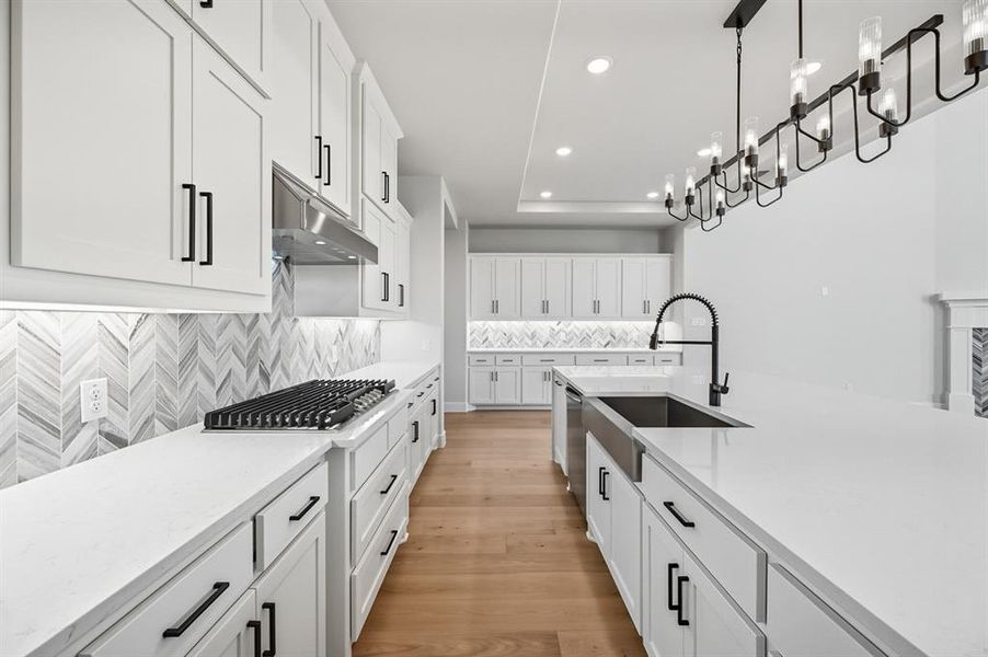 Kitchen with white cabinets, light stone counters, backsplash, light wood-type flooring, and recessed lighting