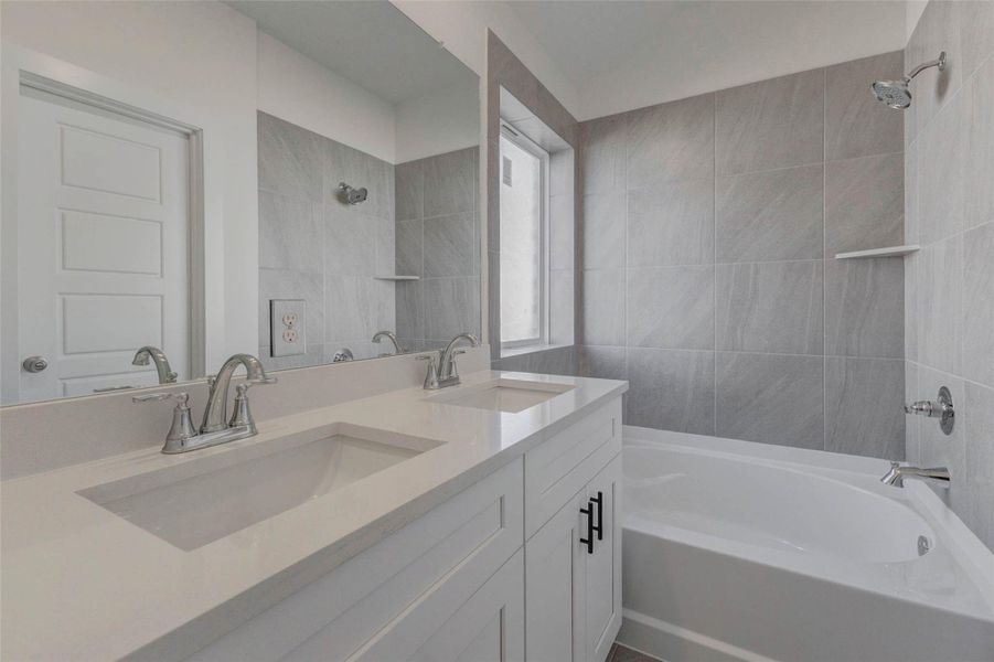 Enjoy everyday luxury in this serene en suite bath featuring modern gray tile, polished chrome fixtures, and a deep soaking tub with shower combo. The dual vanities offer individual space for morning routines, while the large frosted window bathes the room in soft, natural light.