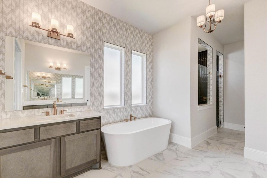 This elegant bathroom features a modern design with a freestanding tub, dual sinks, and stylish lighting. The space is accented by a wall of designer tile and large mirrors, with natural light streaming through frosted windows. Marble-style flooring adds a touch of luxury.