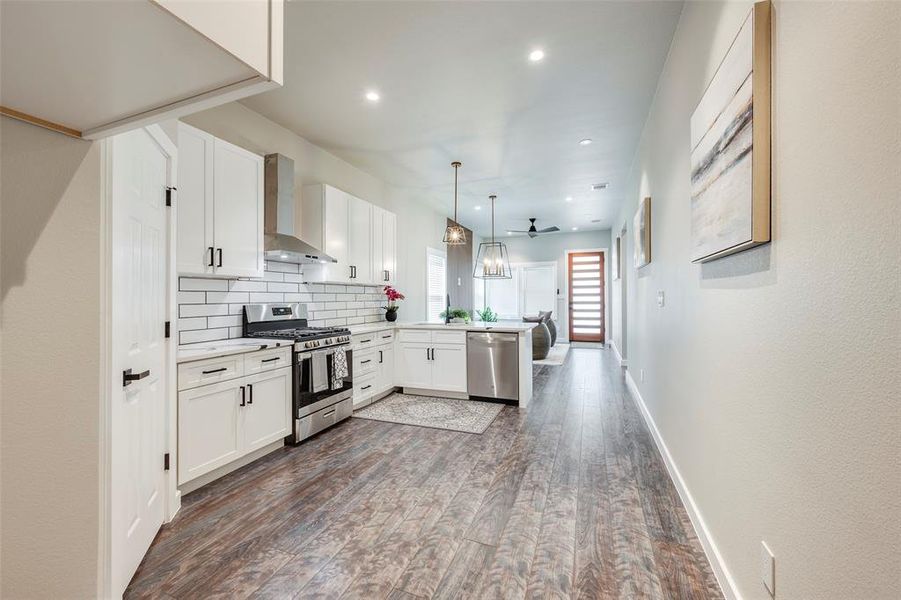 Kitchen with white cabinets, appliances with stainless steel finishes, backsplash, dark wood finished floors, and pendant lighting