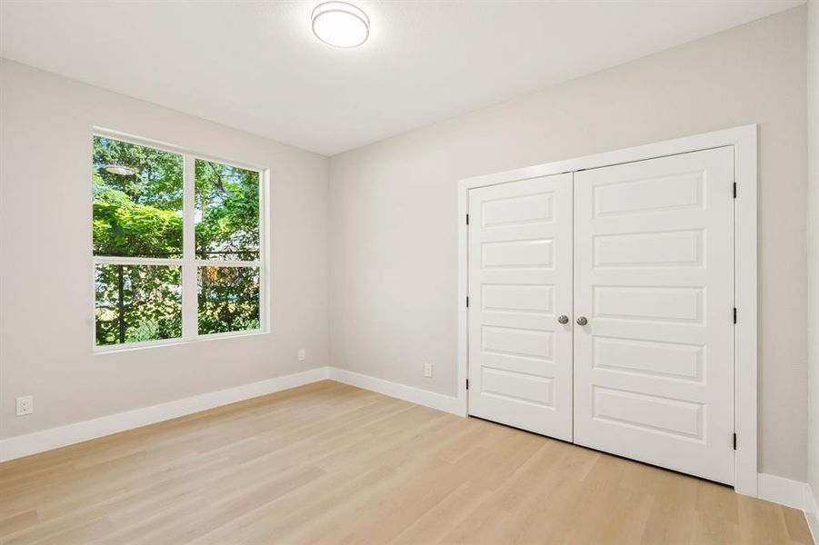 Bright room featuring a large window, light-toned wood-finish flooring, white baseboards, and a flush mount ceiling light Bright room featuring a large window, light-toned wood-finish flooring, white baseboards, and a flush mount ceiling light