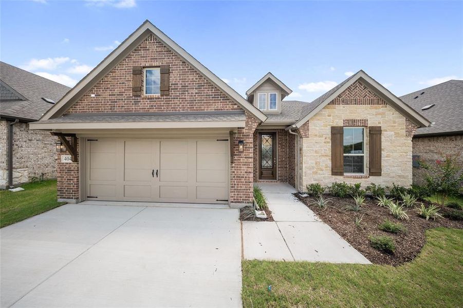 View of front facade featuring a shingled roof, a garage, concrete driveway, brick siding, and stone siding