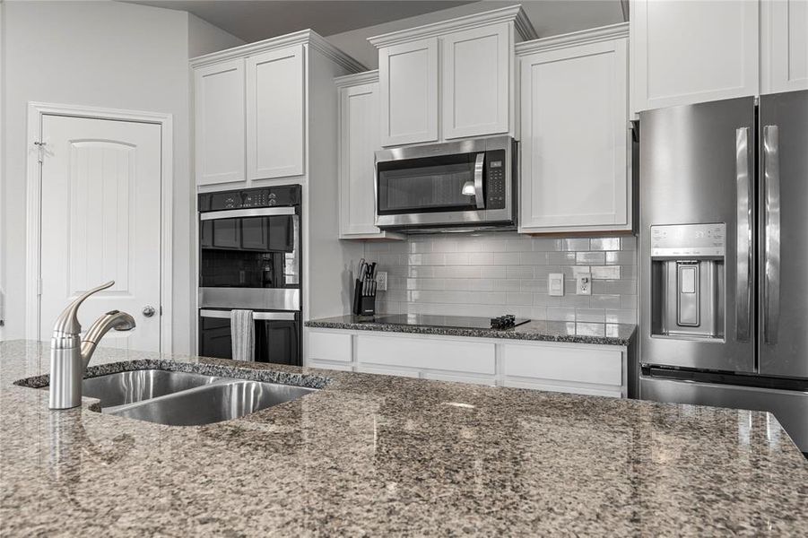 Kitchen featuring tasteful backsplash, stainless steel appliances, dark stone countertops, and white cabinets