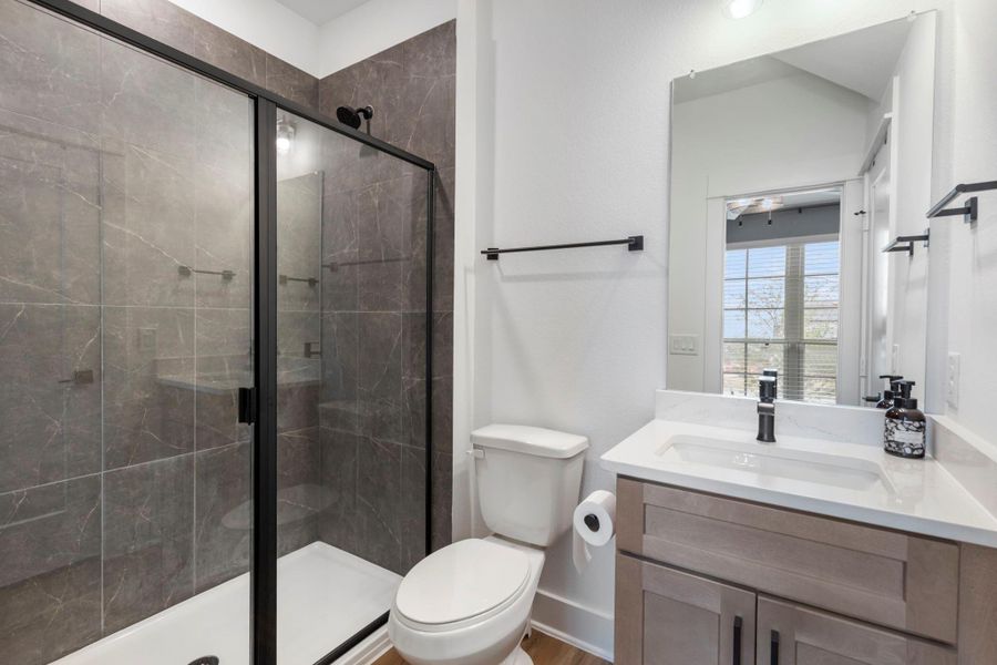 Modern bathroom downstairs full bath with a sleek glass-enclosed shower, elegant dark tile, and a bright vanity area featuring a spacious countertop and large mirror. Modern bathroom downstairs full bath with a sleek glass-enclosed shower, elegant dark tile, and a bright vanity area featuring a spacious countertop and large mirror.